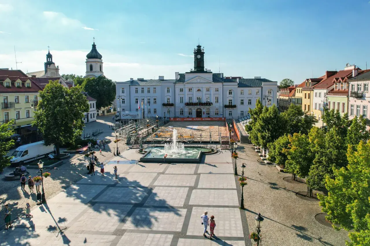Stary Rynek Płock z ratuszem i fontanną w centrum. W tle widać kościoły i kolorowe kamienice.