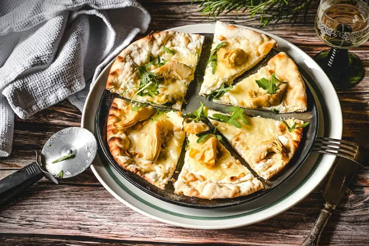 Eine köstliche Pizza Bianca mit Artischocken, Rucola und Pinienkernen, bereit zum Genießen.