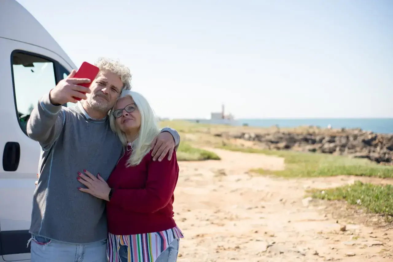 Para singli po 50-tce, którzy szukają przygód, idealne są wycieczki kamperem. Para robi sobie selfie na tle morza.