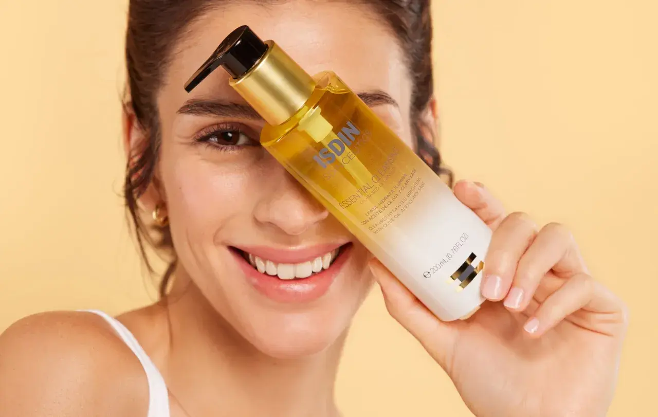 Mujer sonriente sostiene una botella de aceite de ducha ISDIN.