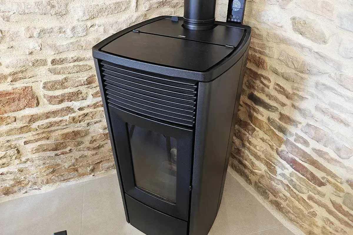 Poêle à granulés noir moderne, avec écran de contrôle, adossé à un mur de pierres. Apprenez comment éteindre un poêle à granulé en toute sécurité.