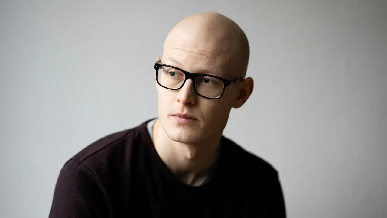 En skallig man med glasögon, Emil Kjær Voss, tittar bortåt med en fundersam blick.
