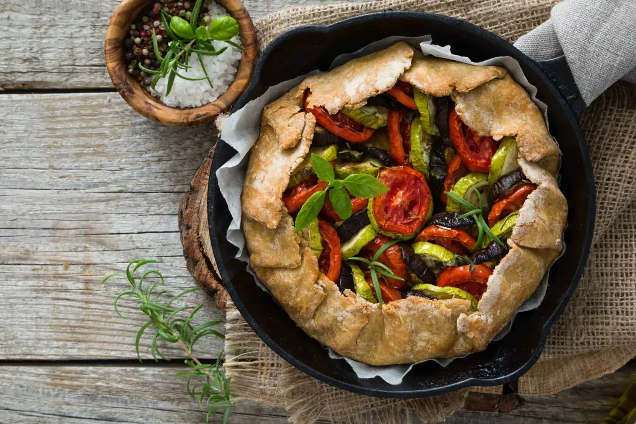 Une rustique quiche aux légumes, garnie de tomates, courgettes et aubergines, prête à être dégustée.