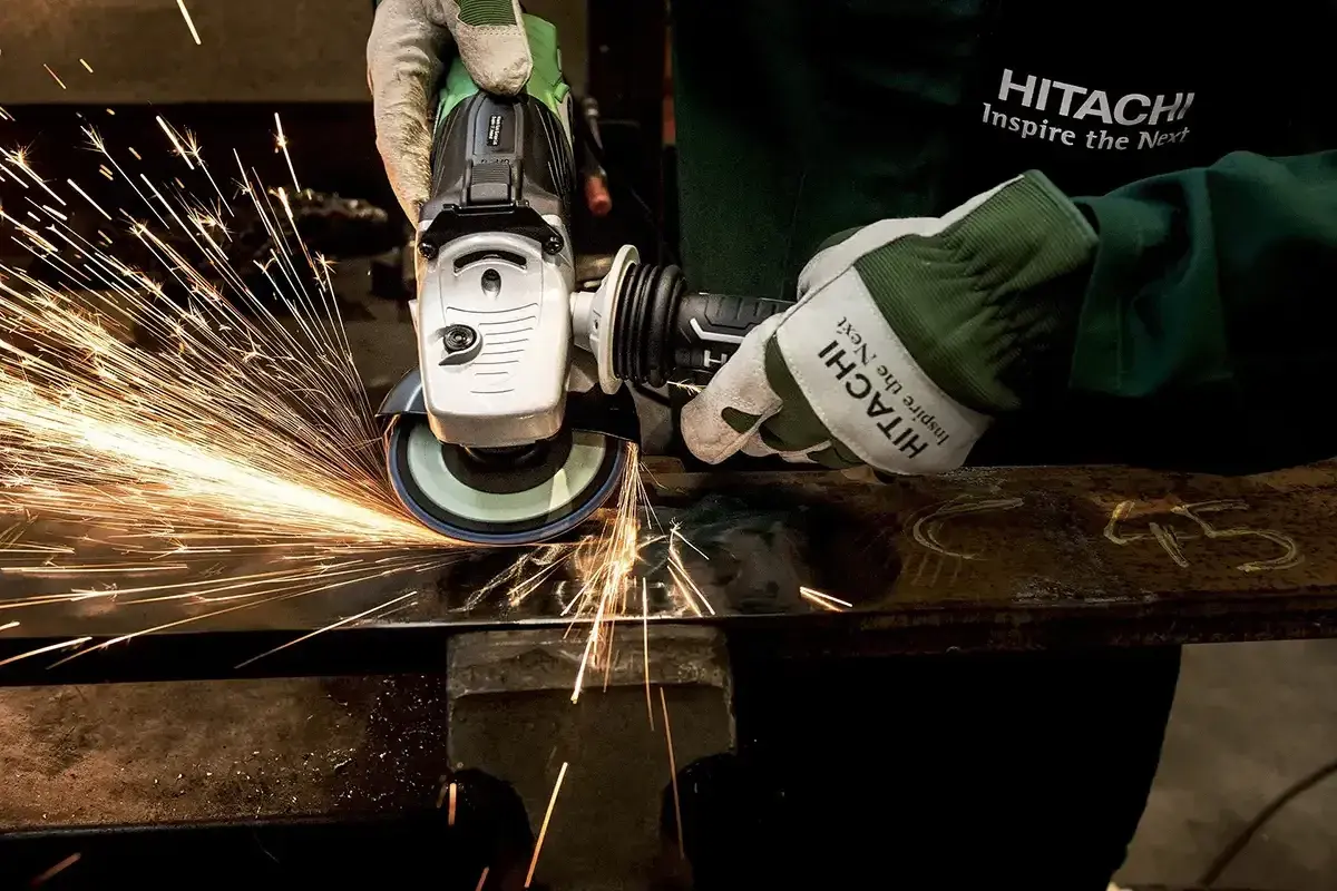 Ręce w rękawicach Hitachi wykonują polerowanie szlifierką kątową, sypią się iskry.