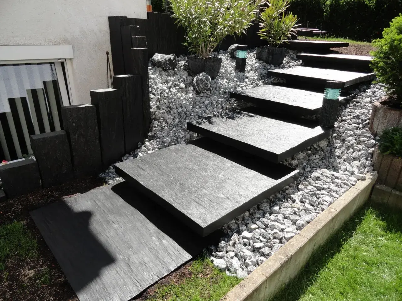 Moderner gartenweg am hang ohne stufen, mit dunklen Steinplatten und Kiesbett.
