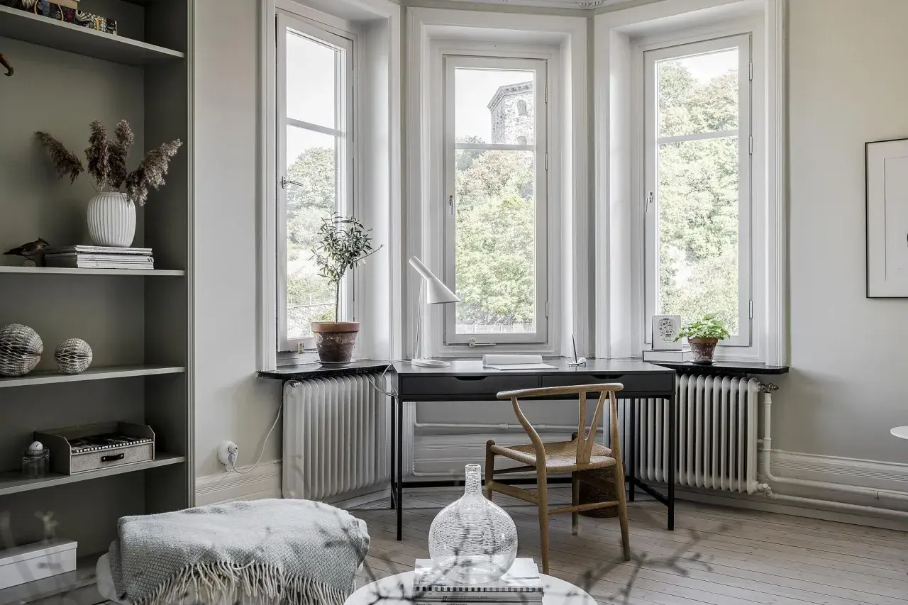 Scrivania con vista finestra, un angolo studio luminoso con sedia in legno e piante.