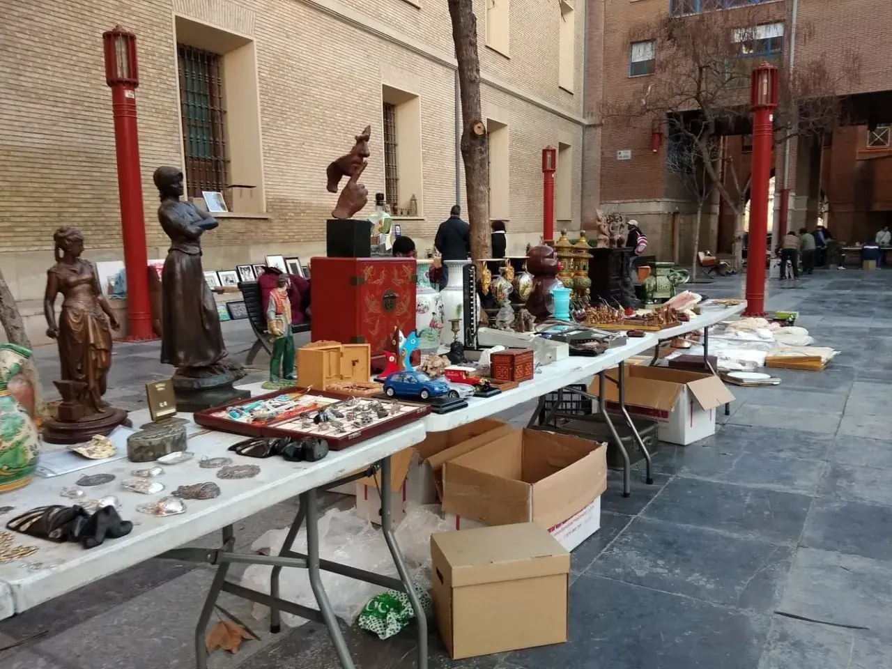 Mercado de antigüedades en Zaragoza con estatuas, jarrones y objetos curiosos en mesas al aire libre.