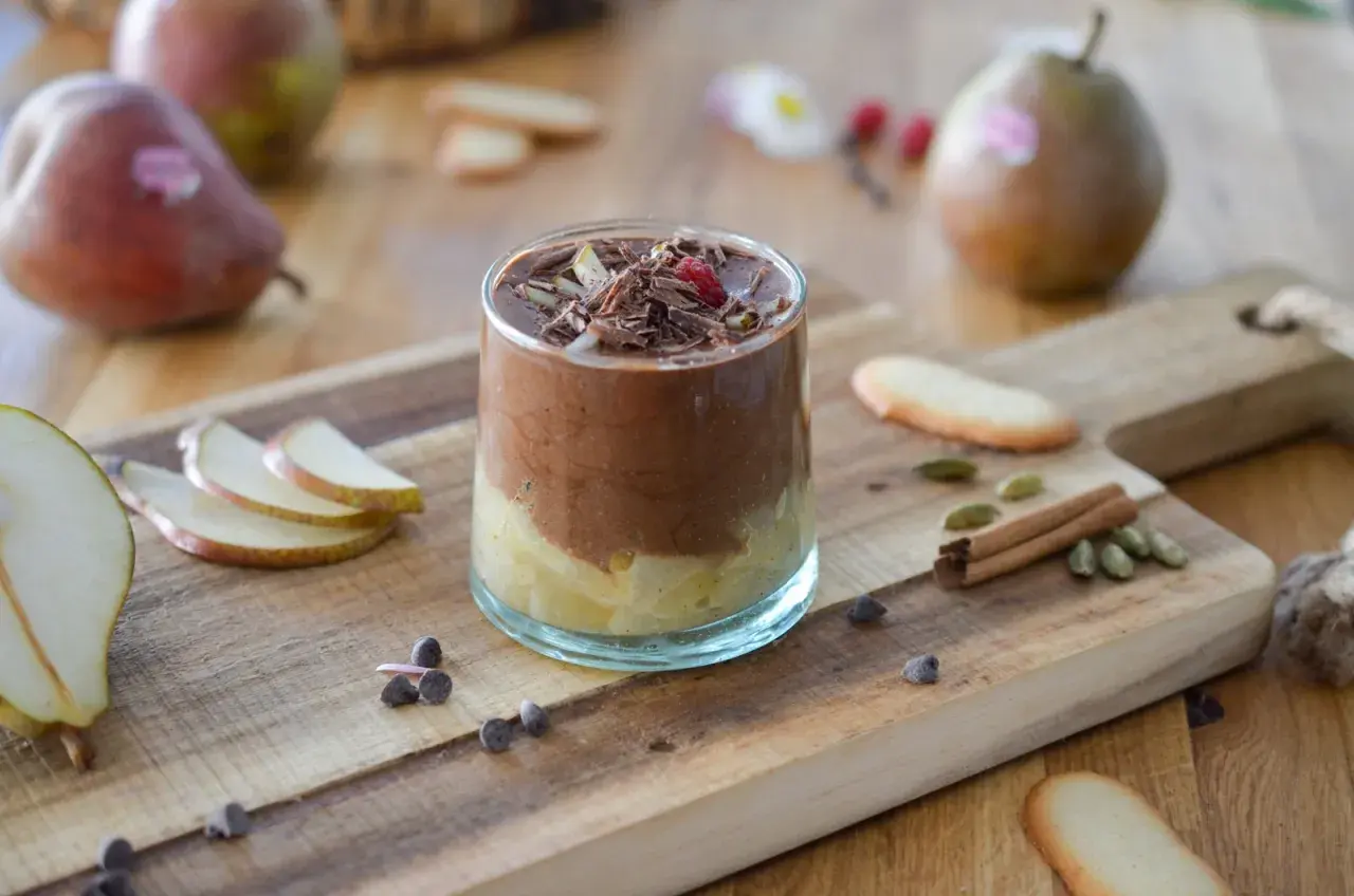 Délicieuse recette mousse poire chocolat, garnie de copeaux de chocolat et d'une framboise. Poires fraîches et épices sur fond de bois.
