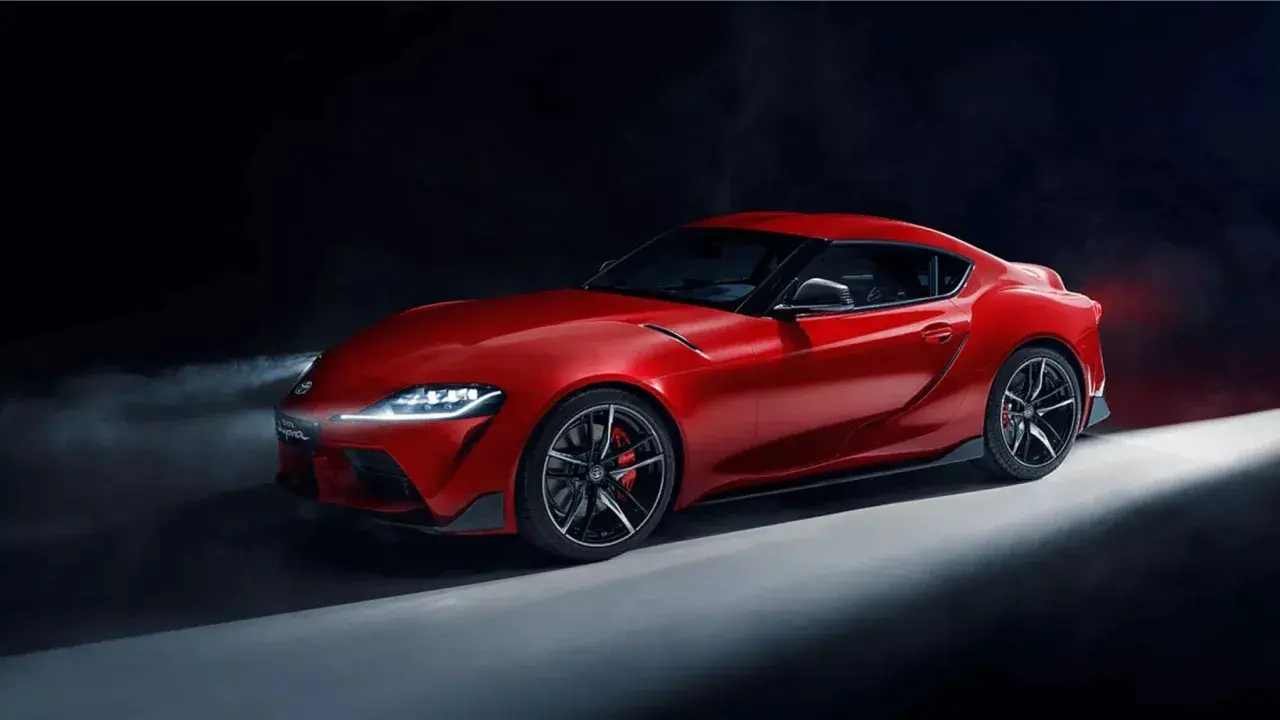 Un deportivo Toyota Supra rojo brillante, con luces encendidas y humo detrás, listo para la acción.