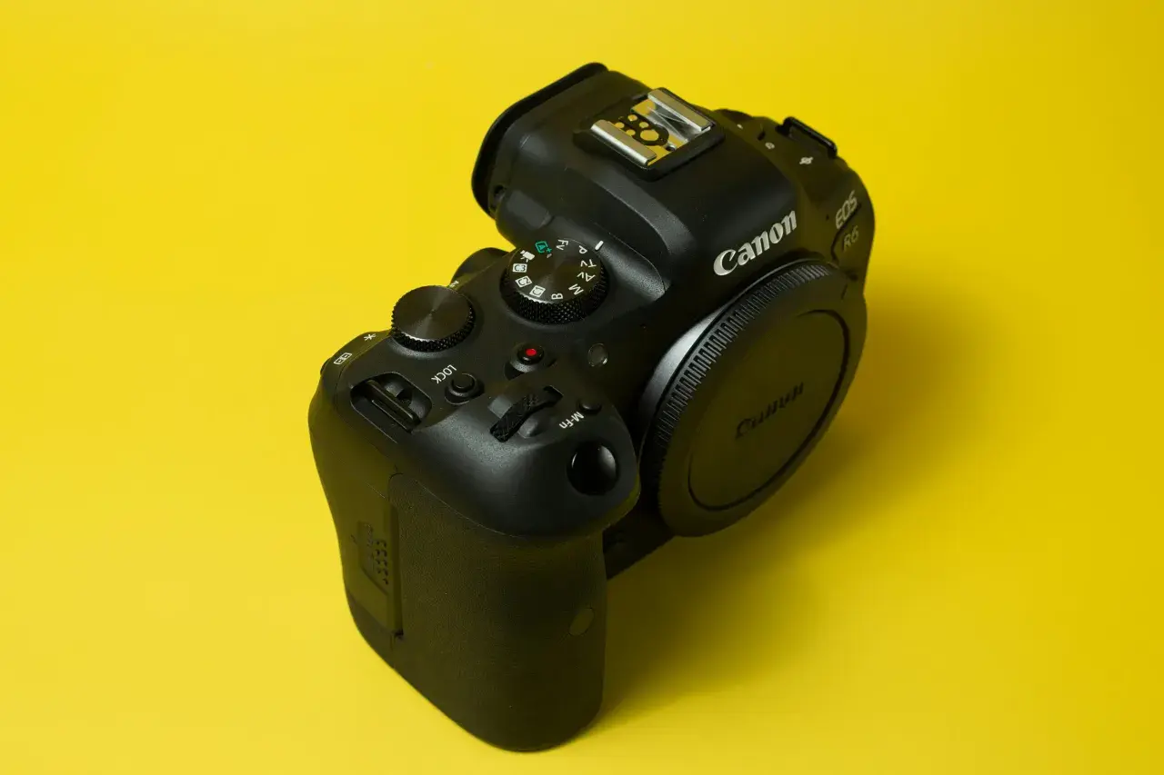 Czarny aparat Canon EOS R6 na żółtym tle. Pokrętło trybów pozwala na preselekcję czasu, ułatwiając kontrolę nad ekspozycją.