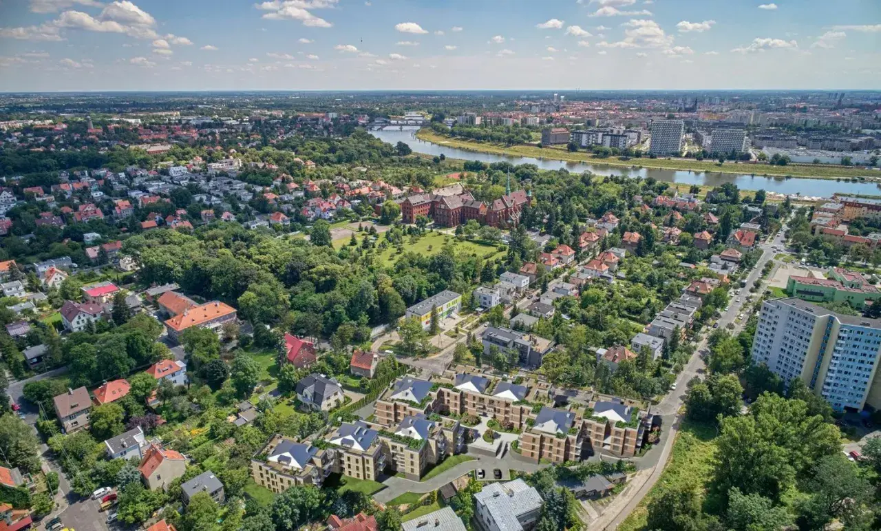 Nowoczesne osiedle w otoczeniu zieleni, z widokiem na rzekę i miasto. W oddali widać zabytkowe budynki i nowe apartamentowce. To idealne miejsce dla osób ceniących spokój i bliskość natury, a jednocześnie dostęp do miejskich atrakcji.