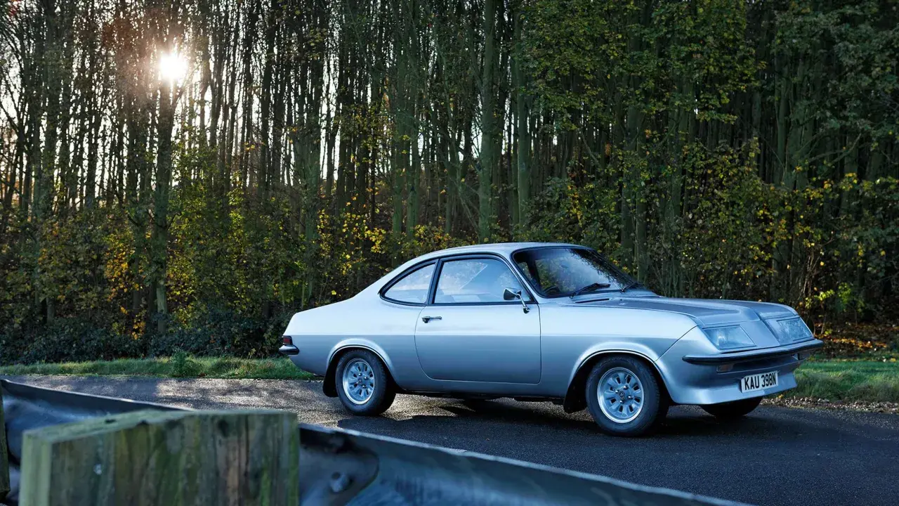 Silver Vauxhall Firenza på en väg kantad av träd. Solen skiner genom grenarna.