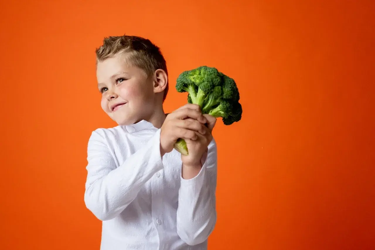 Bambino sorridente con un broccolo, un ortaggio salutare. Non è un legume, ma è ottimo per la salute!