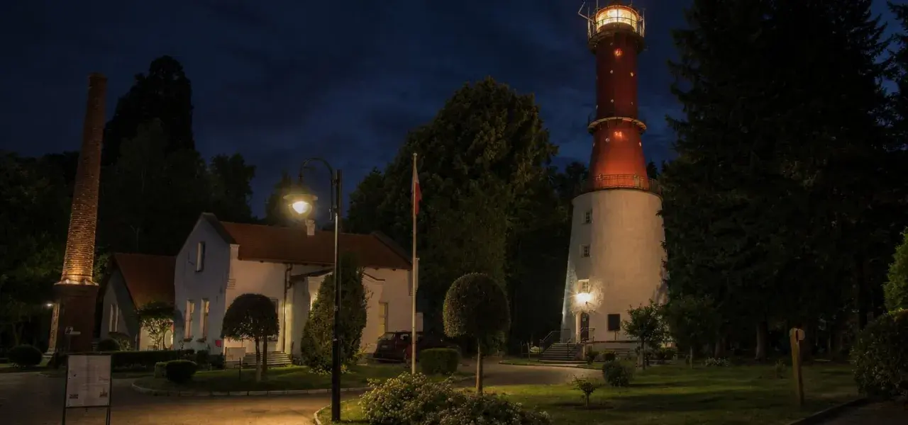 Latarnia morska Jastrzębia Góra nocą, z oświetlonym budynkiem i charakterystyczną czerwoną wieżą.
