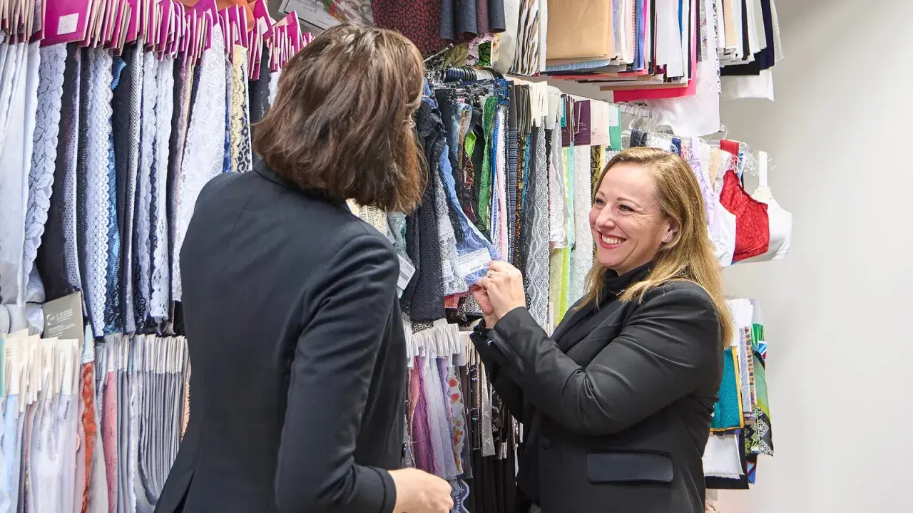Deux femmes choisissent des échantillons de tissus, dont une belle dentelle en fibre artificielle, dans un atelier de mode.