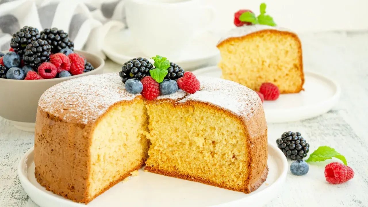 Torta soffice allo yogurt greco, decorata con frutti di bosco freschi e una spolverata di zucchero a velo.