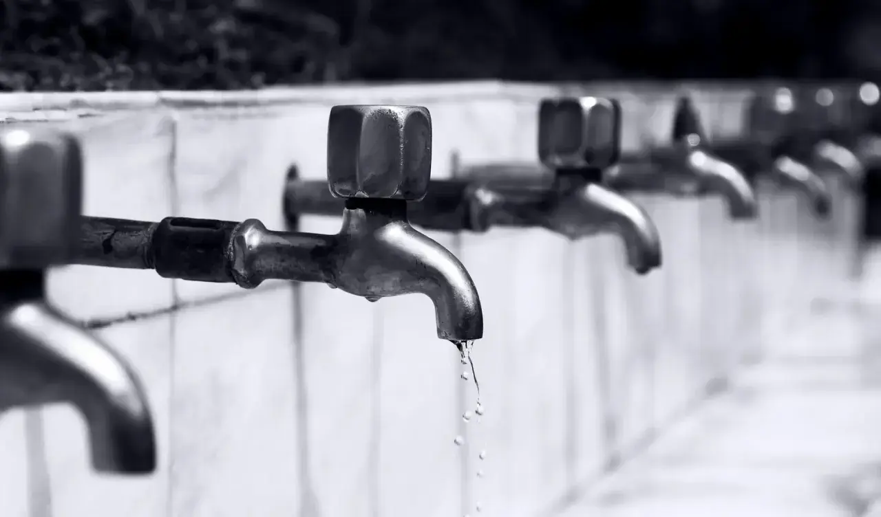 Reihe von Wasserhähnen, aus denen Tropfen fallen.
