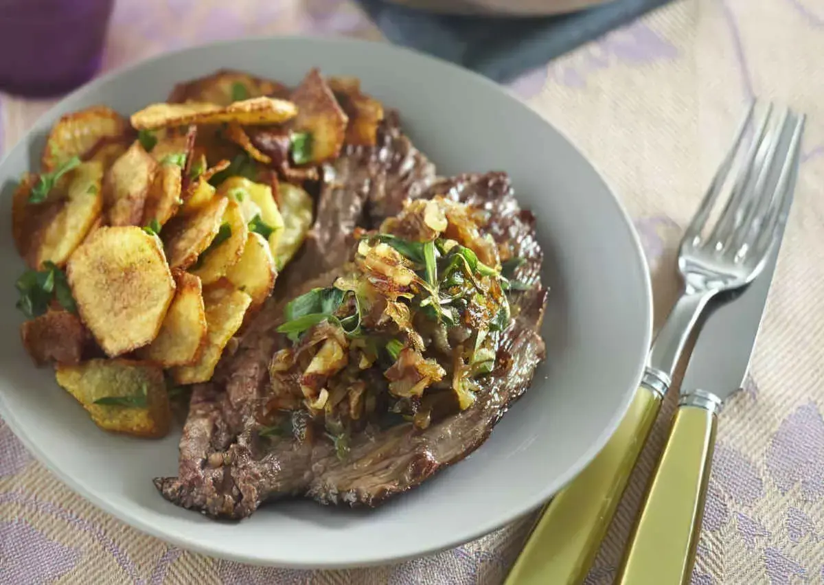 Une assiette de bavette à l'échalote, accompagnée de pommes de terre croustillantes et d'herbes fraîches. Un délice visuel et gustatif.