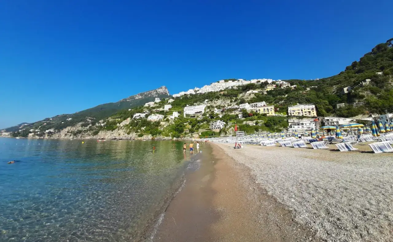 Plage de galets à Vietri sul Mare, Italie, avec des maisons blanches perchées sur la colline verdoyante et la mer bleue étincelante.