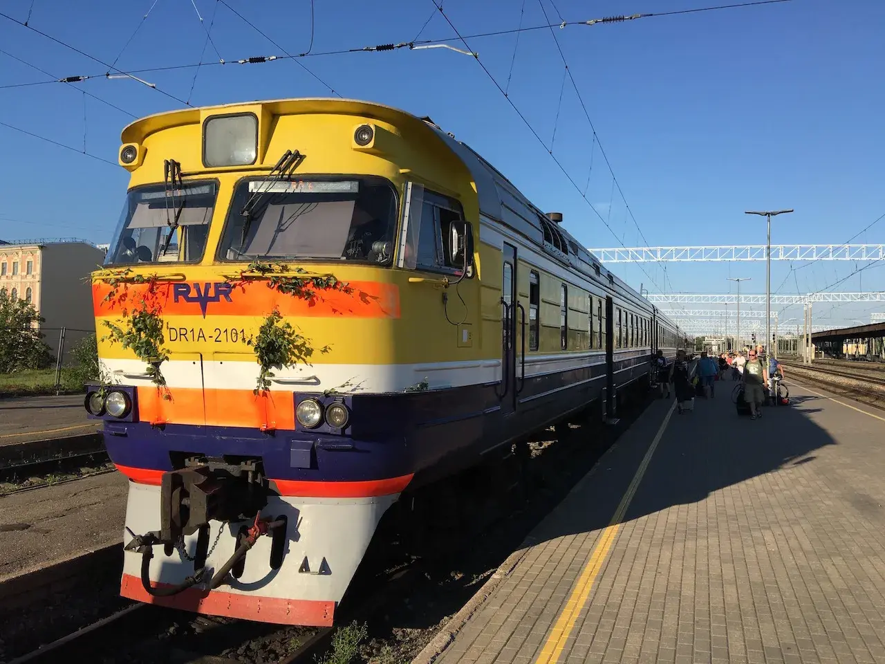 Gelber Zug mit grüner Deko am Bahnhof, bereit für die Fahrt von Riga nach Tallinn.