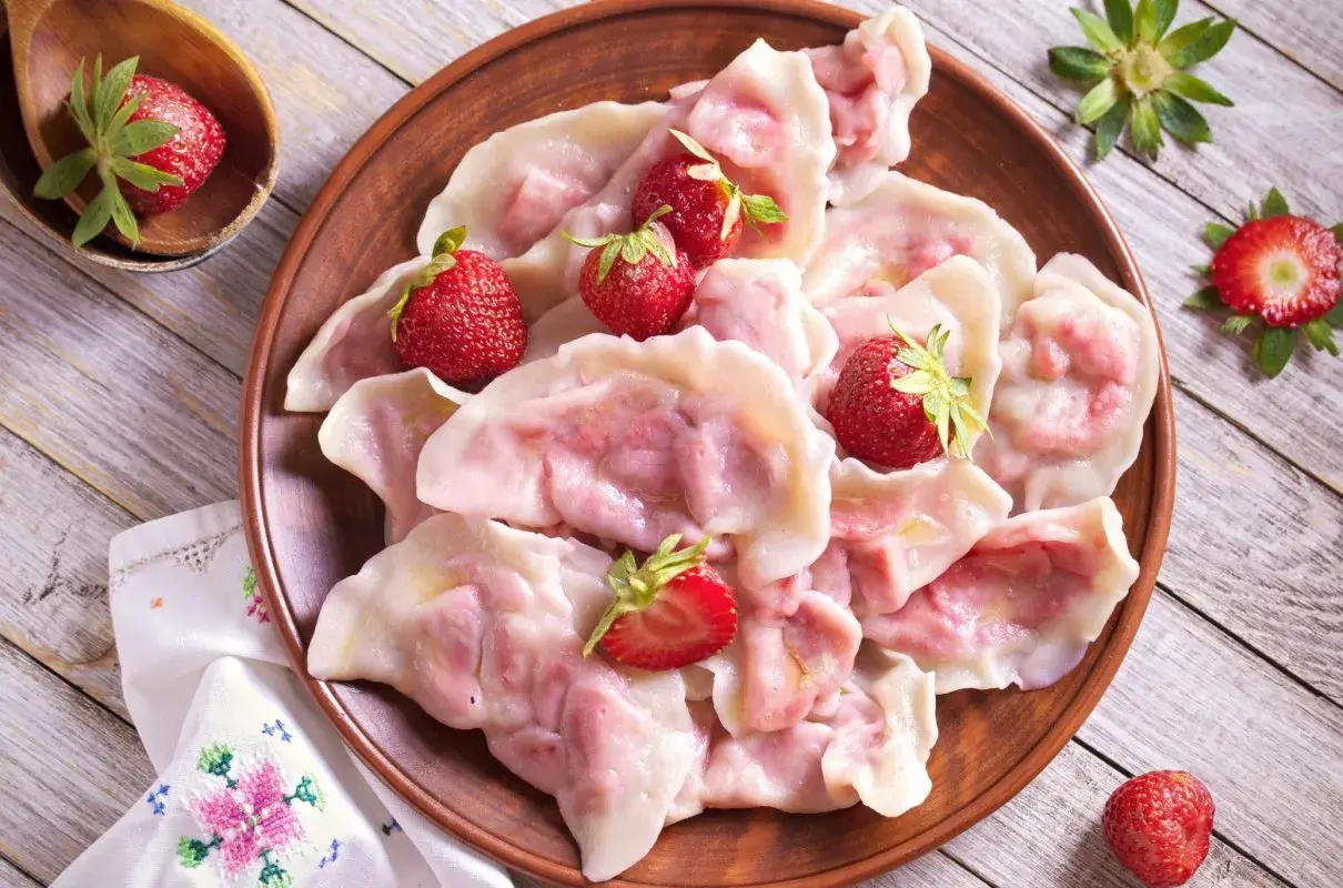 Pyszne pierogi z truskawkami, ozdobione świeżymi owocami, wyglądają apetycznie na glinianym talerzu.