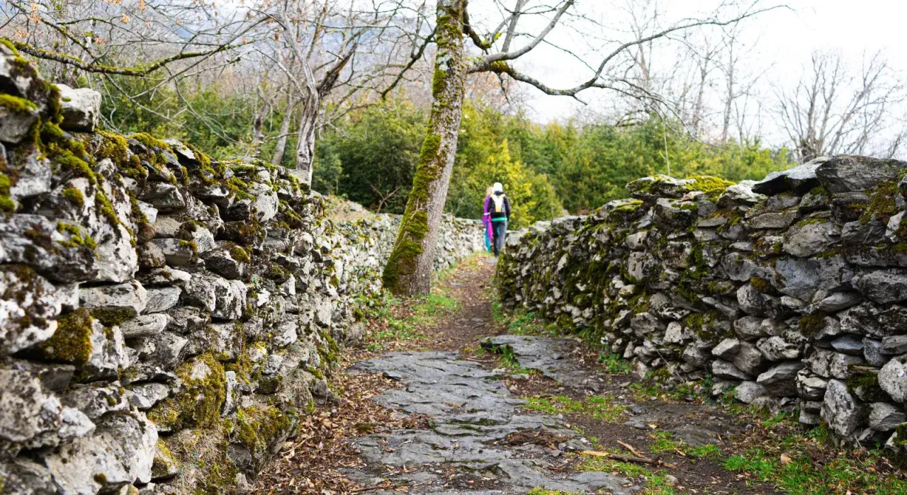 Sendero de piedra cubierto de musgo, parte de la ruta Garganta de Escuain. Dos excursionistas avanzan por el camino.