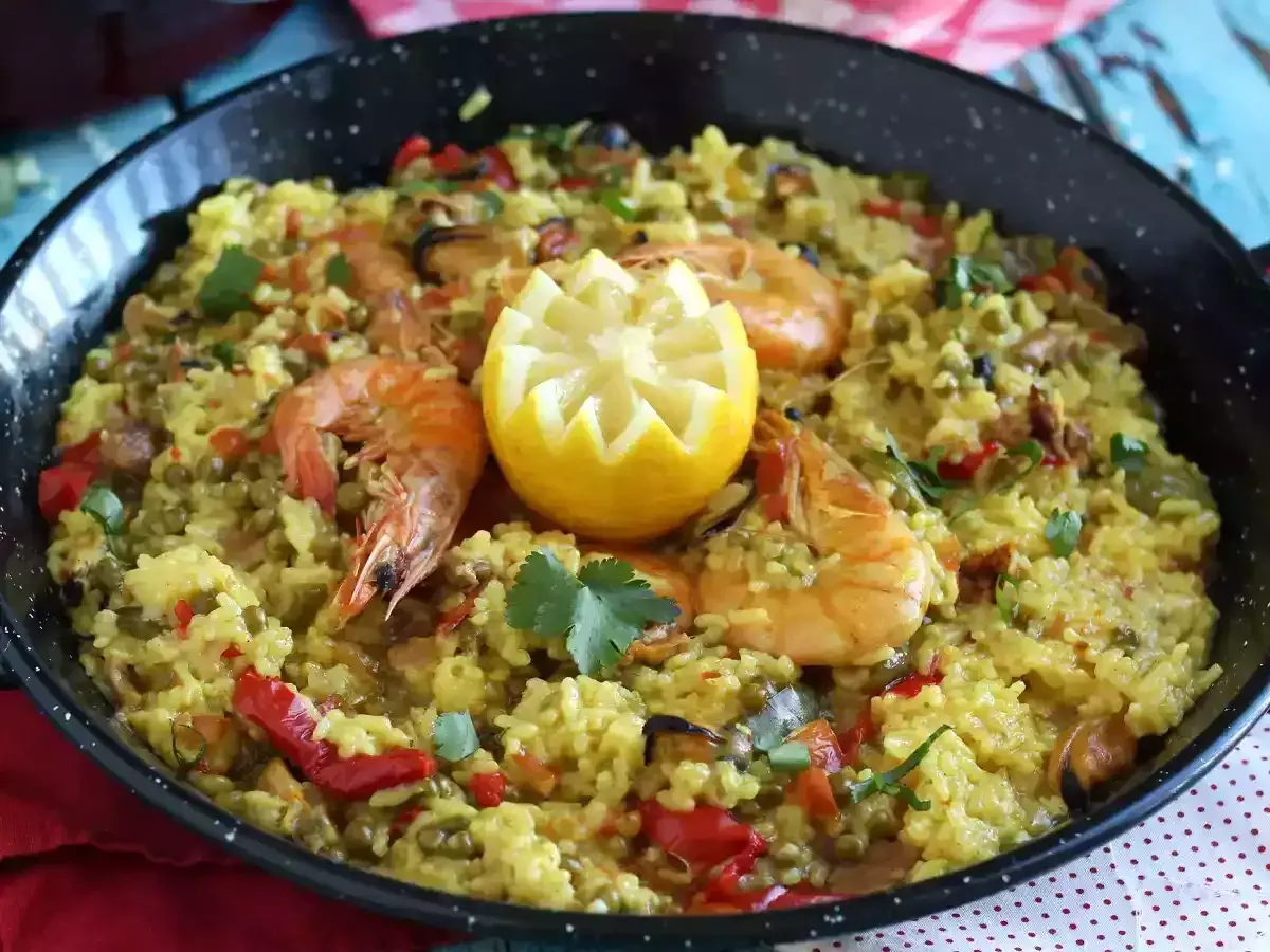 Arroz con pollo y marisco en paellera, adornado con limón y perejil. Un festín de sabores.