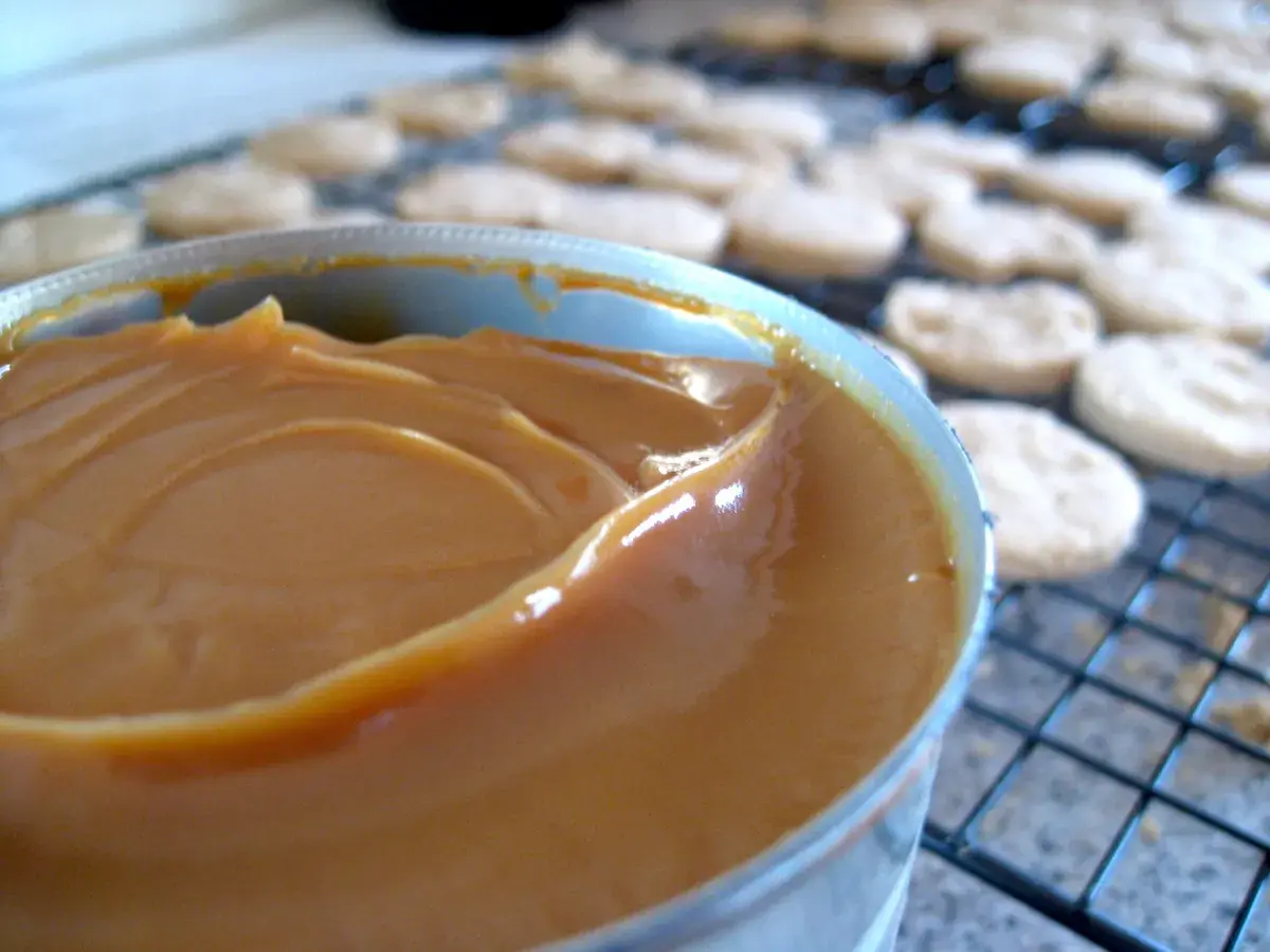 Un pot de confiture de lait onctueuse, prêt à garnir des biscuits secs disposés sur une grille.