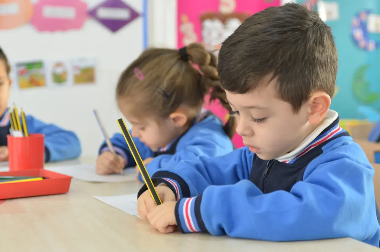 Niños concentrados en sus cuadernos, un momento de aprendizaje y adaptación en el aula.