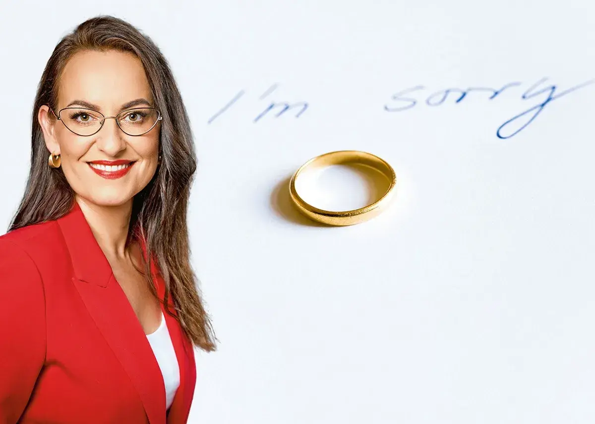 Uśmiechnięta prawniczka w czerwonej marynarce obok obrączki i napisu "I'm sorry". Dobry prawnik od rozwodów pomoże przejść przez trudne chwile.