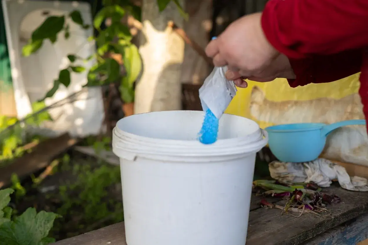 Une main verse une poudre bleue dans un seau blanc. C'est la préparation de la bouillie bordelaise pour protéger les plantes.