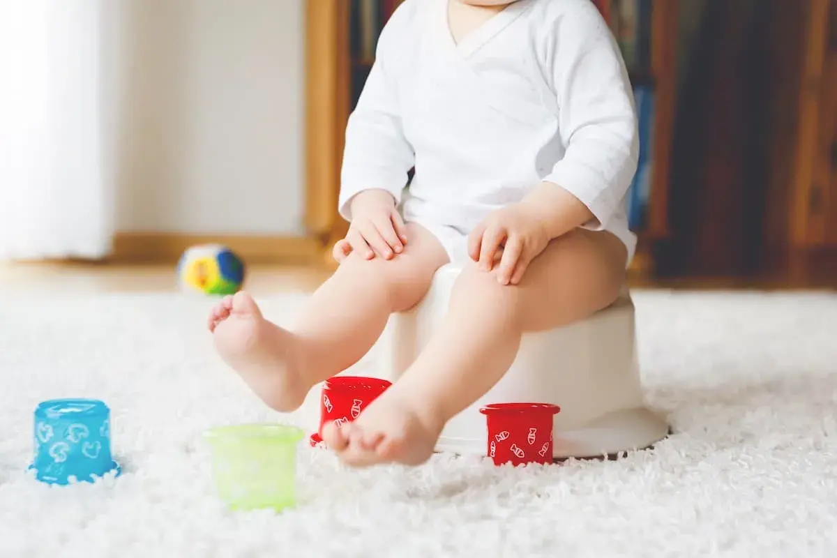 Liten bebis på pottan, redo att sluta med napp. Färgglada leksaker och en mjuk matta skapar en trygg miljö för potträning.