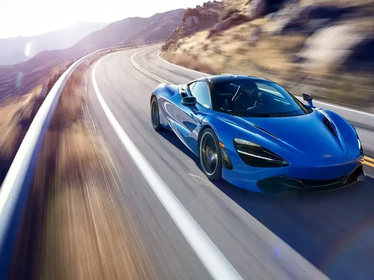 Niebieski McLaren 720S pędzi po krętej górskiej drodze, tworząc rozmyte smugi światła i cienia.