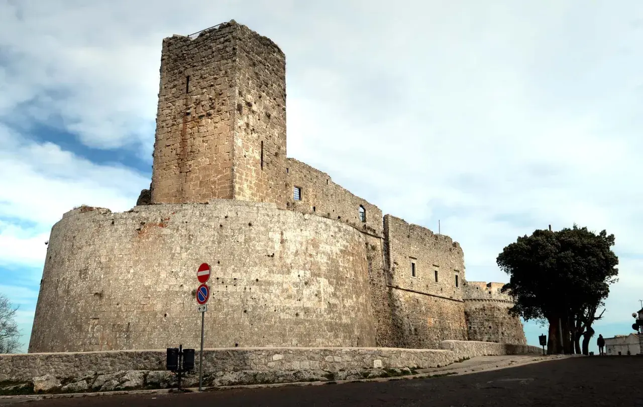 Imponente castello di Monte Sant'Angelo, con mura in pietra grezza e un torrione svettante sotto un cielo nuvoloso.