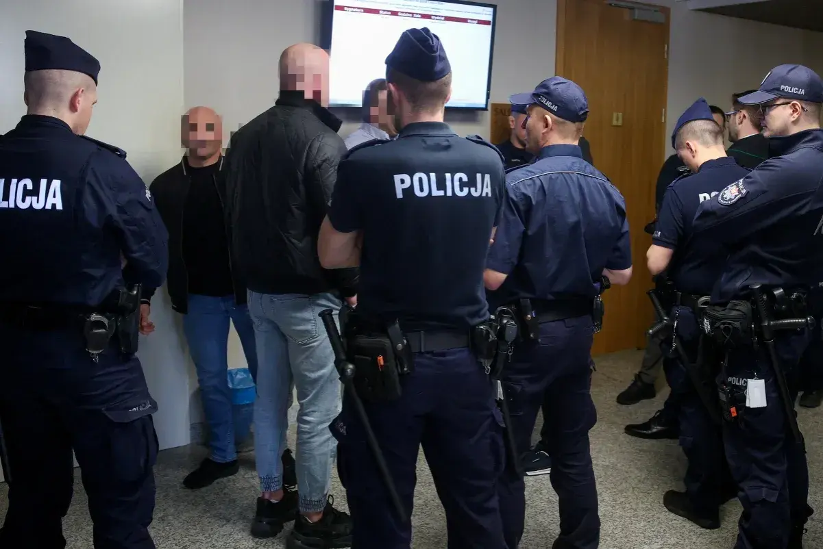 Policjanci otaczają grupę mężczyzn, wśród których mogą być psycho fans. Wszyscy mają zakryte twarze.