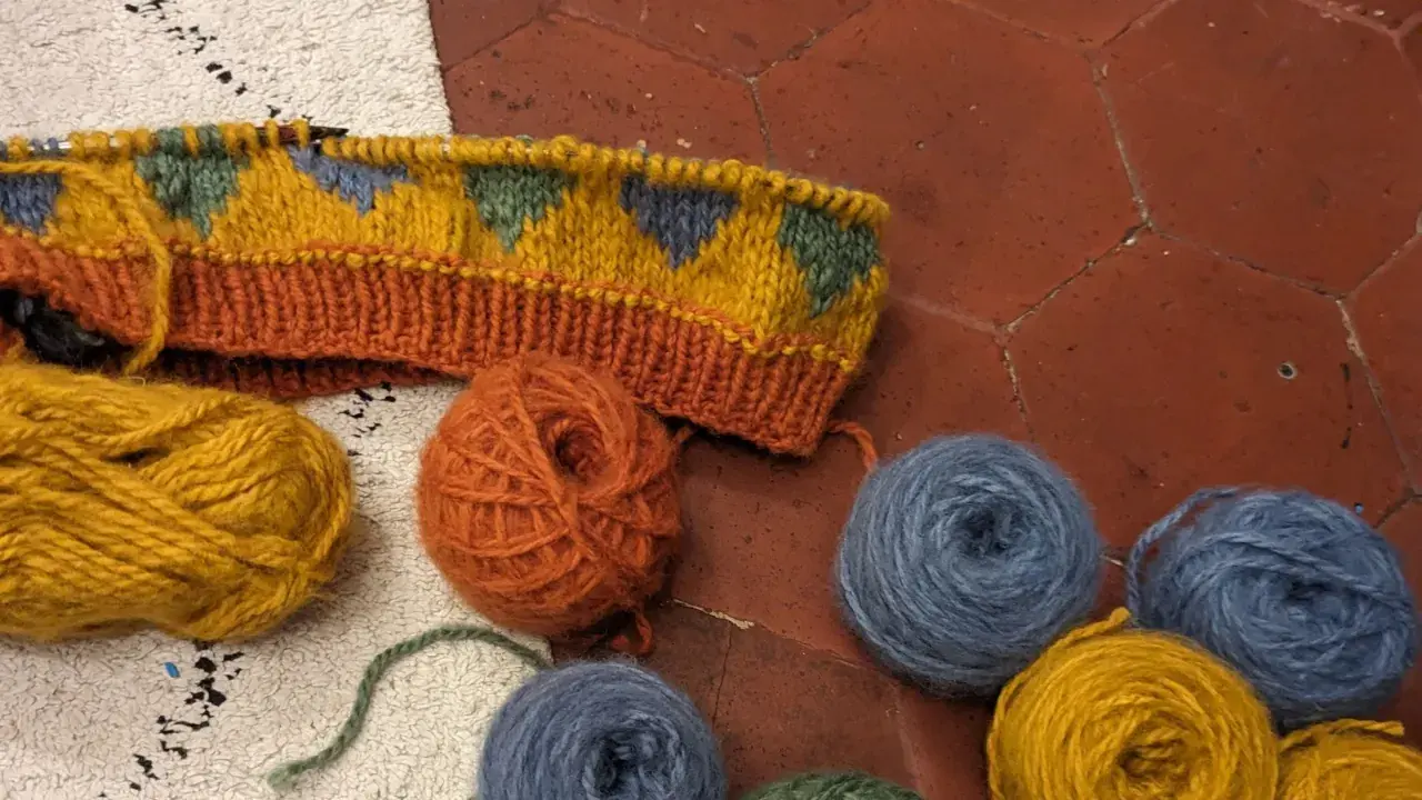 Un tricot jacquard aux motifs géométriques colorés, entouré de pelotes de laine.