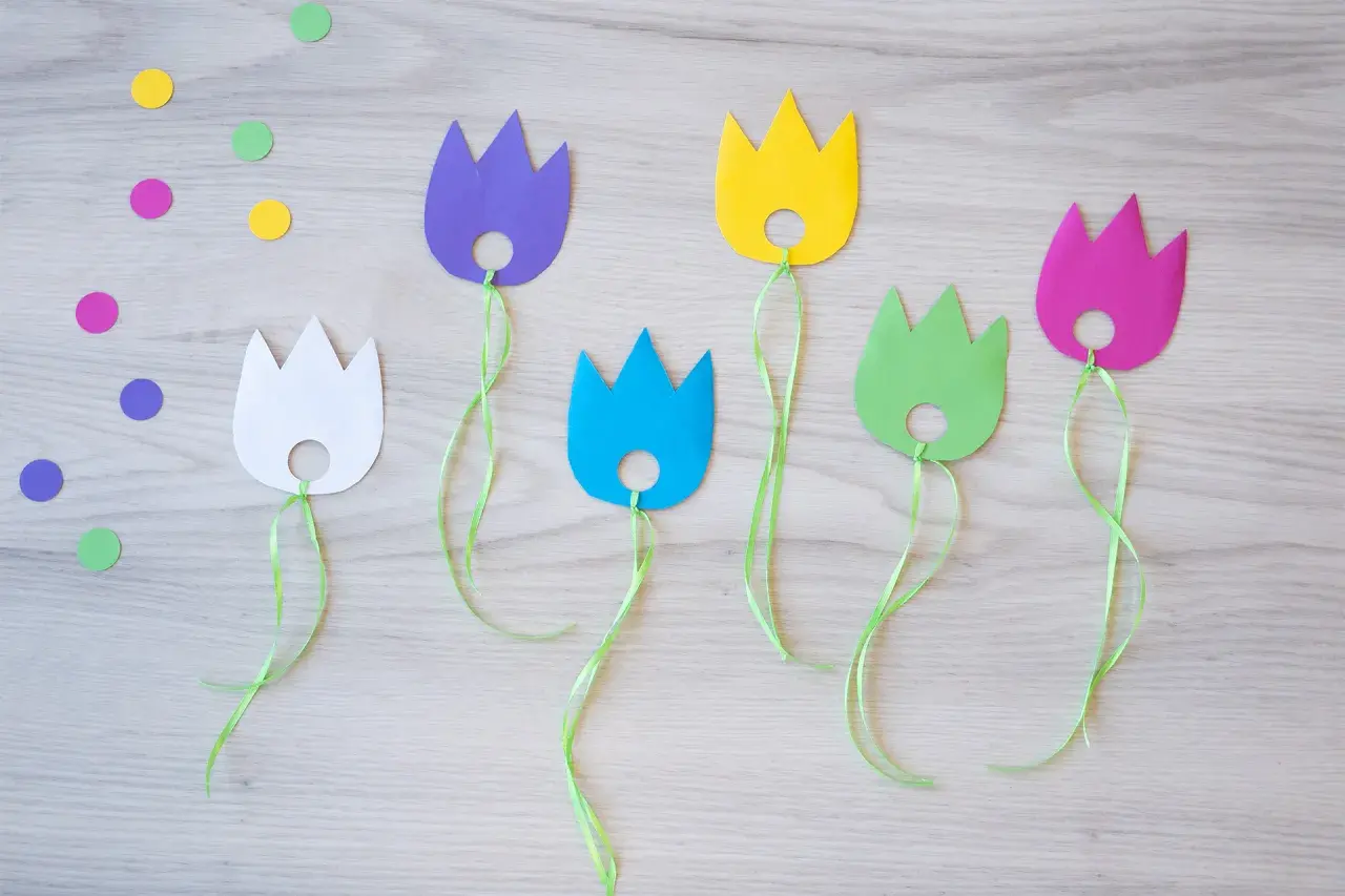 Bunte Papier-Tulpen mit grünen Bändern, perfekt für das Basteln mit Kindern. Bunte Tupfen liegen verstreut.