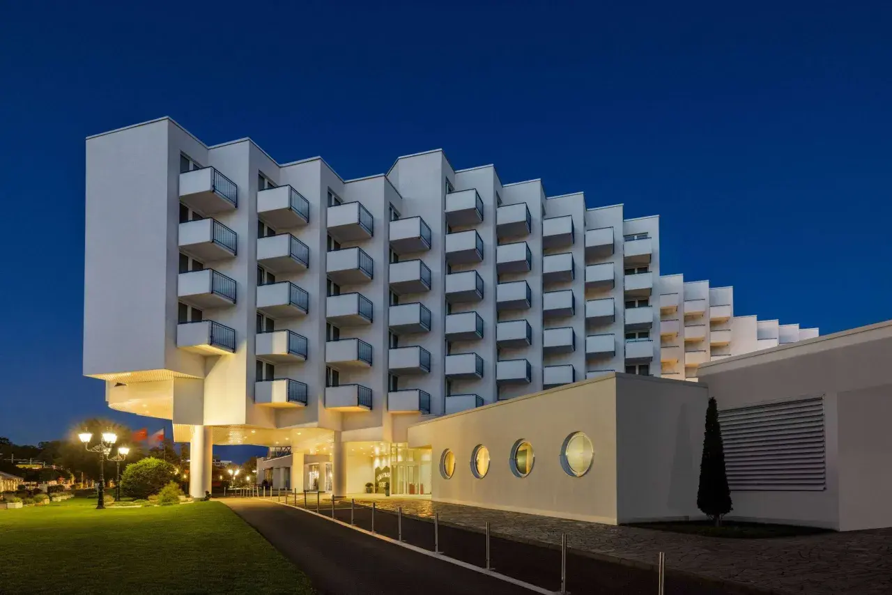 Nowoczesny hotel Amber Baltic w Międzyzdrojach o architekturze z balkonami w kształcie schodków, oświetlony wieczorem.