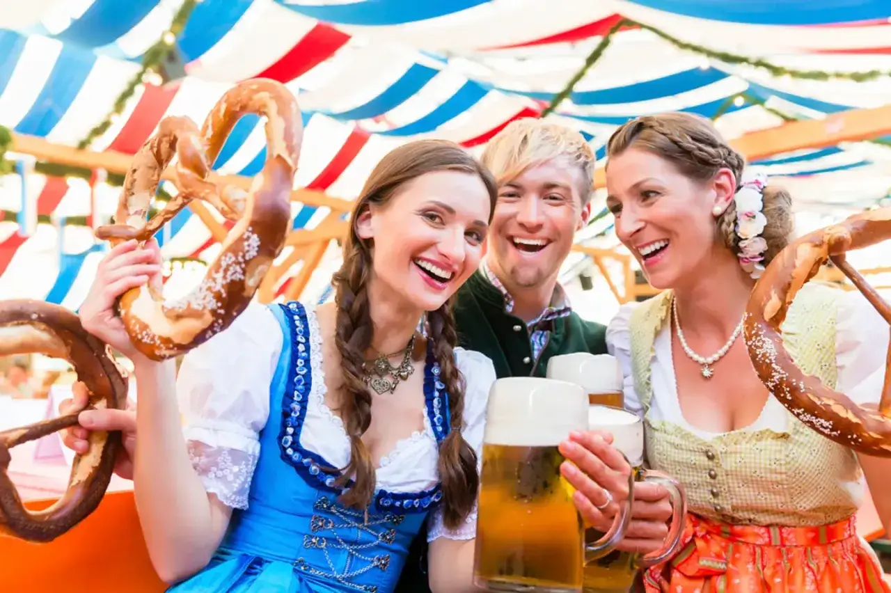 Trois amis joyeux célèbrent à l'Oktoberfest, un lieu festif, avec des bretzels géants et de la bière.