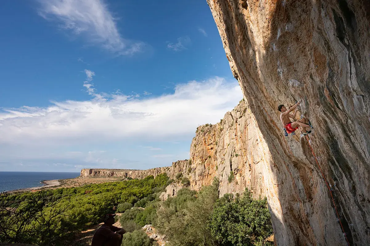 Un grimpeur défie la falaise en Sicile, avec la mer et la végétation en toile de fond. L'escalade sicile offre des vues spectaculaires.