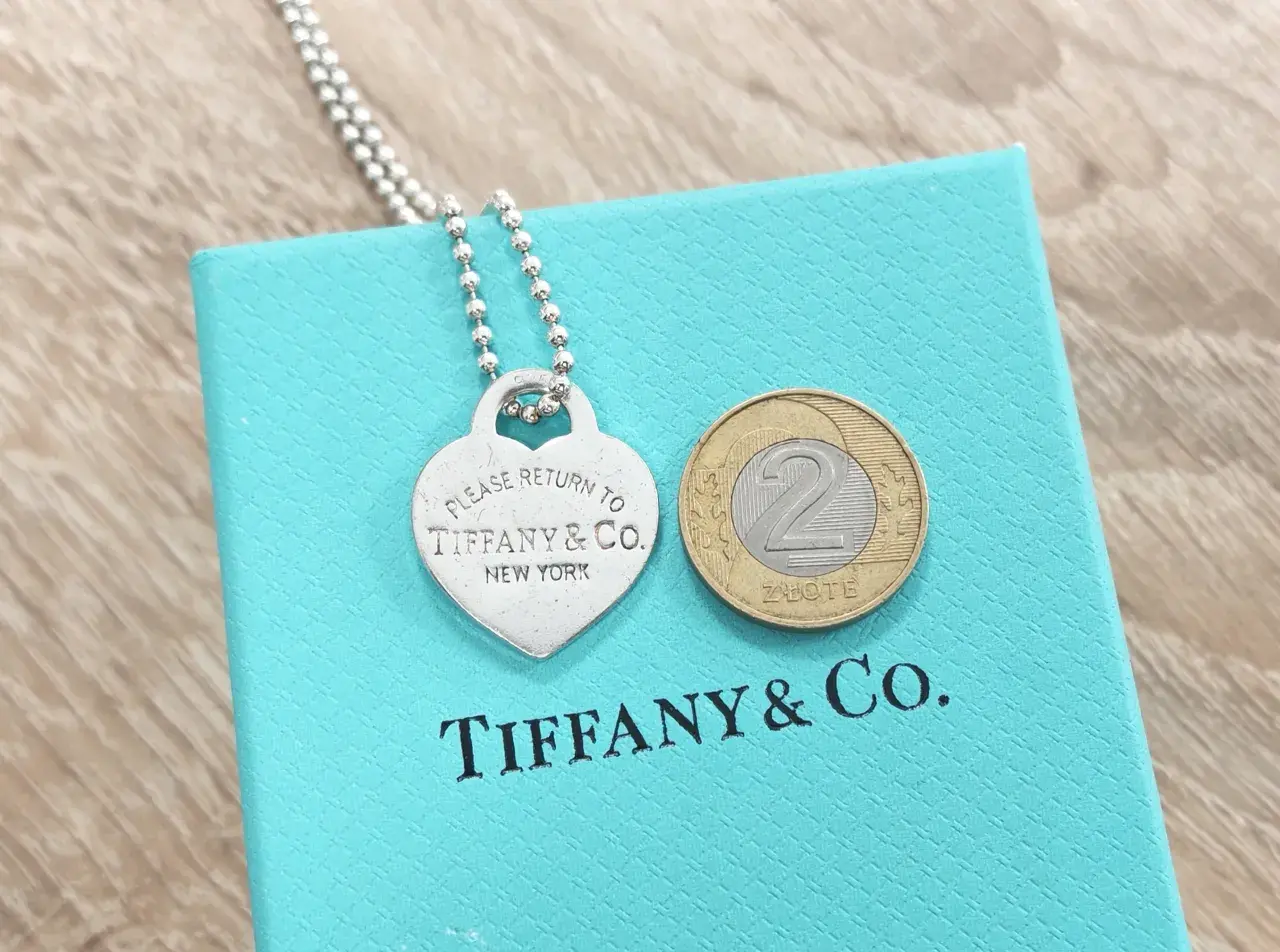 Srebrne serce z napisem "Please Return to Tiffany & Co. New York" na turkusowym pudełku Tiffany & Co. z monetą 2 złote.