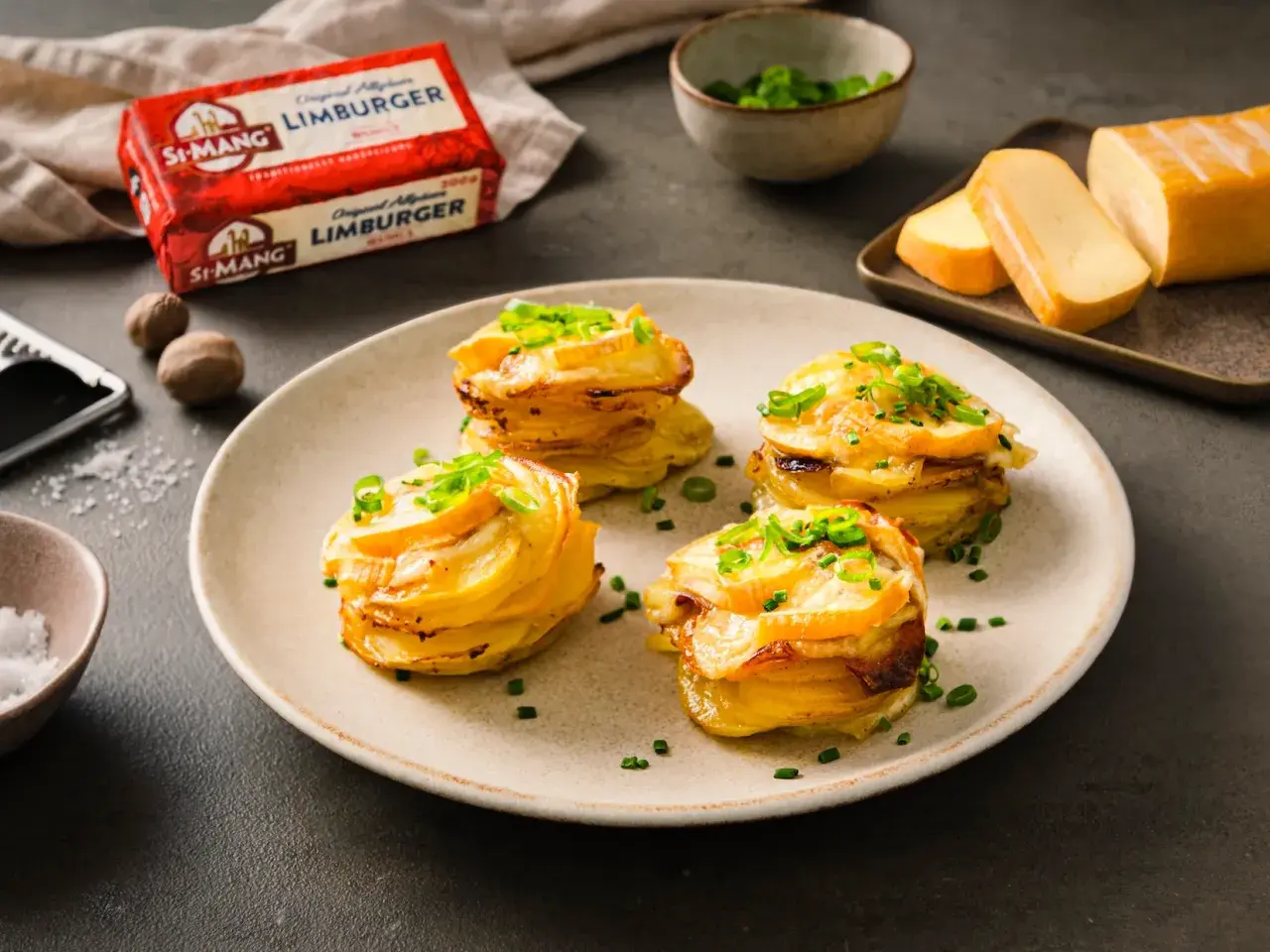 Gestapelte Kartoffeln mit geschmolzenem Käse und Schnittlauch. Daneben ein Block Limburger Käse, bereit für ein Romadur-Gericht.