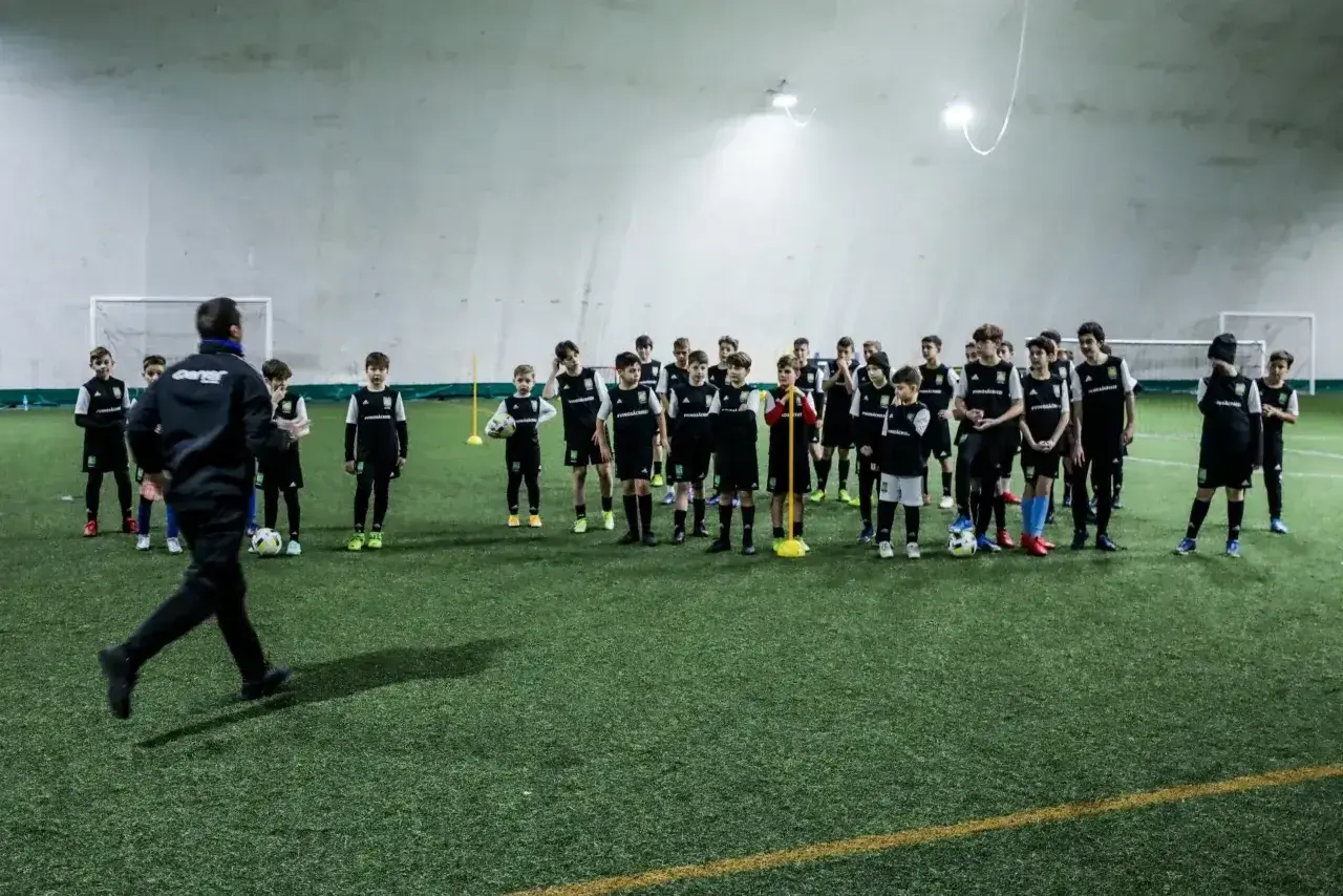 Trener prowadzi trening piłkarski metodą Coerver Coaching, instruując młodych zawodników na boisku.