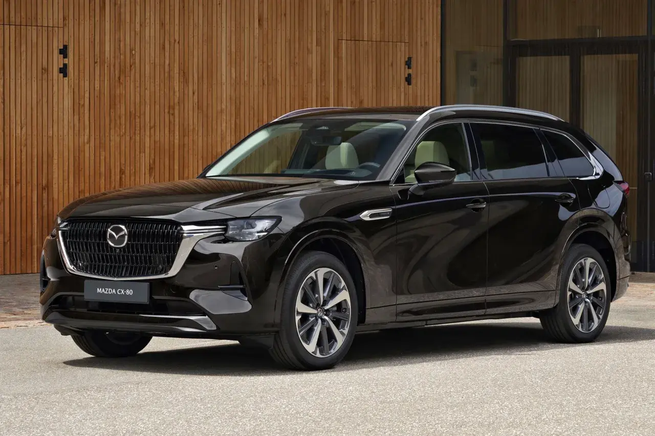 Elegancka, czarna Mazda CX-80 SUV stoi przed nowoczesnym budynkiem z drewnianą elewacją.