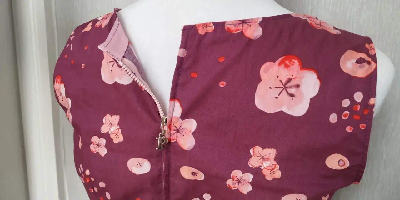 A plum-colored dress with a floral print features a centered zipper with a silver "P" charm.