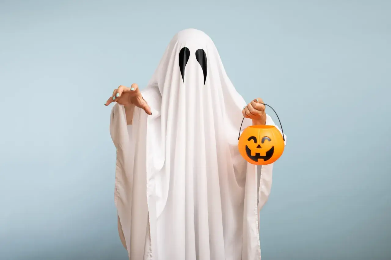 Bambino con costume da fantasma fai da te, tiene un cestino di caramelle a forma di zucca.