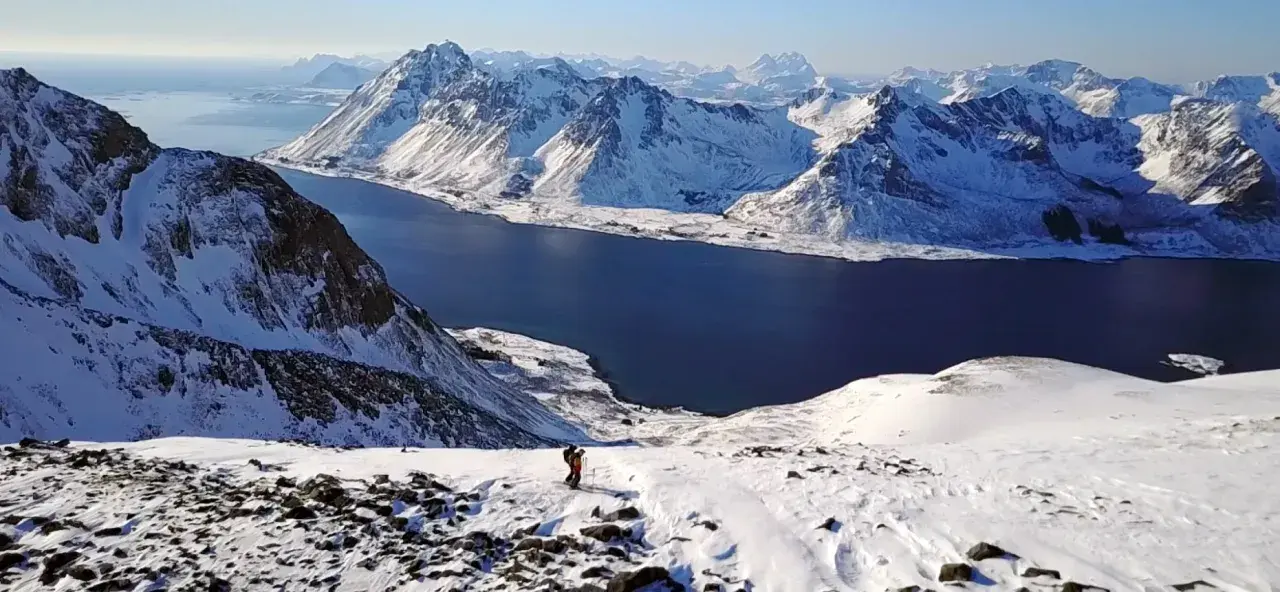 Ein Skifahrer genießt die atemberaubende Aussicht auf die schneebedeckten Berge und das tiefblaue Meer im **Lofoten Winter**.