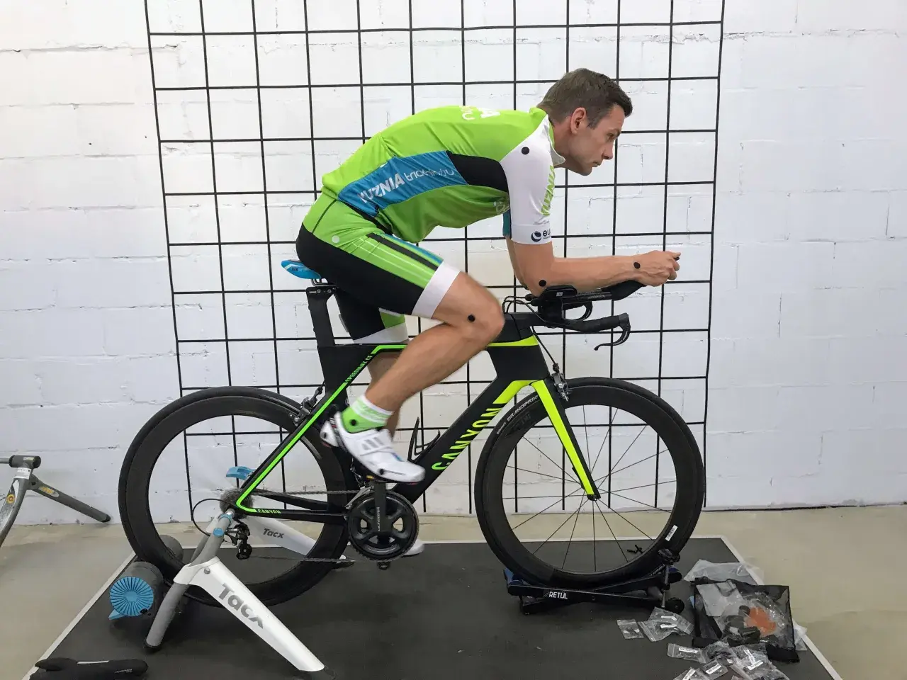 Mężczyzna w stroju kolarskim na rowerze stacjonarnym podczas sesji bike fitting. Punkty pomiarowe na ciele i rowerze.