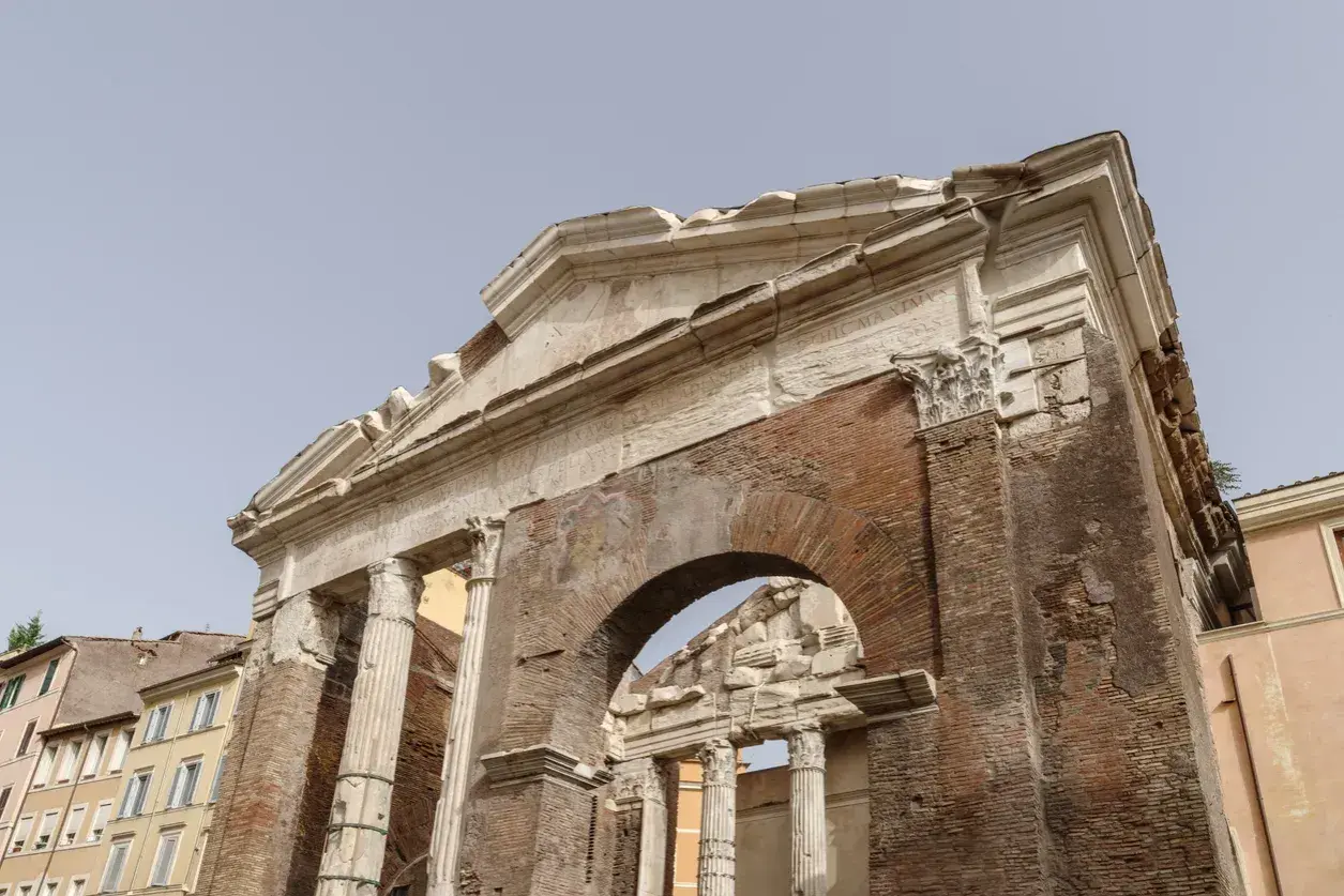 Antica struttura in mattoni e marmo, con colonne e un arco, parte del **Portico di Ottavia**.