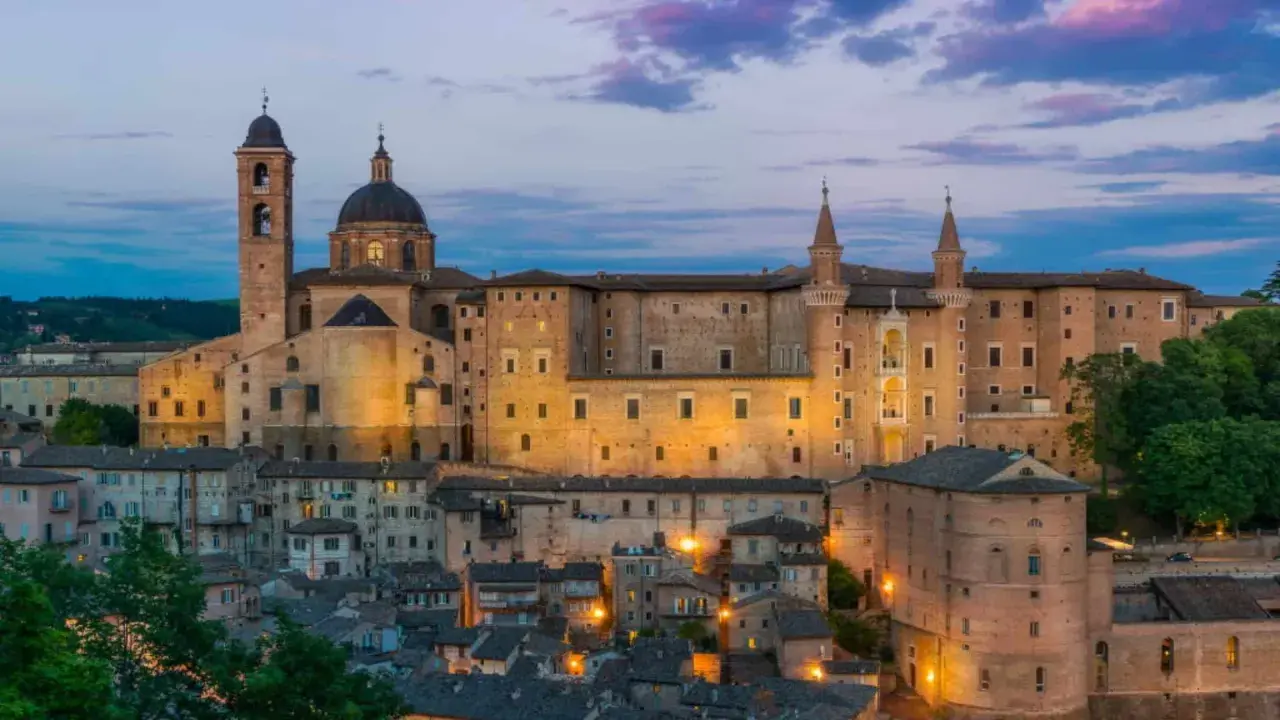 Urbino Natale: il Palazzo Ducale illuminato al crepuscolo, con le sue torri e la cupola, domina la città storica.